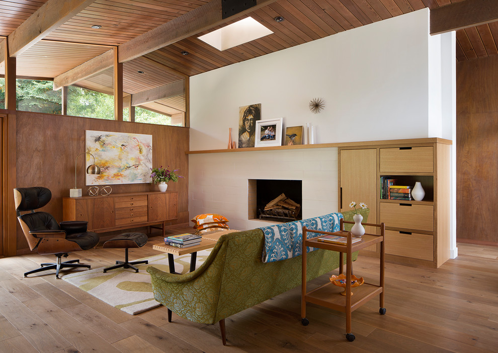 Aménagement d'un salon rétro ouvert avec un mur blanc, un sol en bois brun, une cheminée double-face, un manteau de cheminée en carrelage et un sol marron.