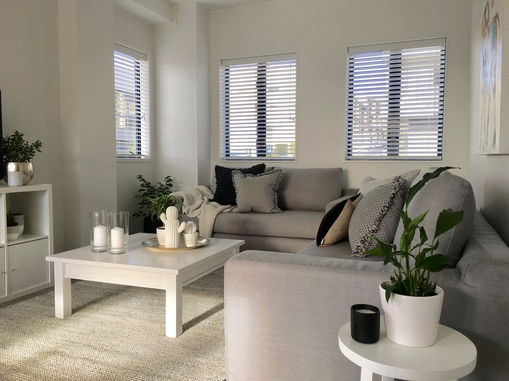 Offenes Modernes Wohnzimmer ohne Kamin mit weißer Wandfarbe, Teppichboden, freistehendem TV und grauem Boden in Auckland
