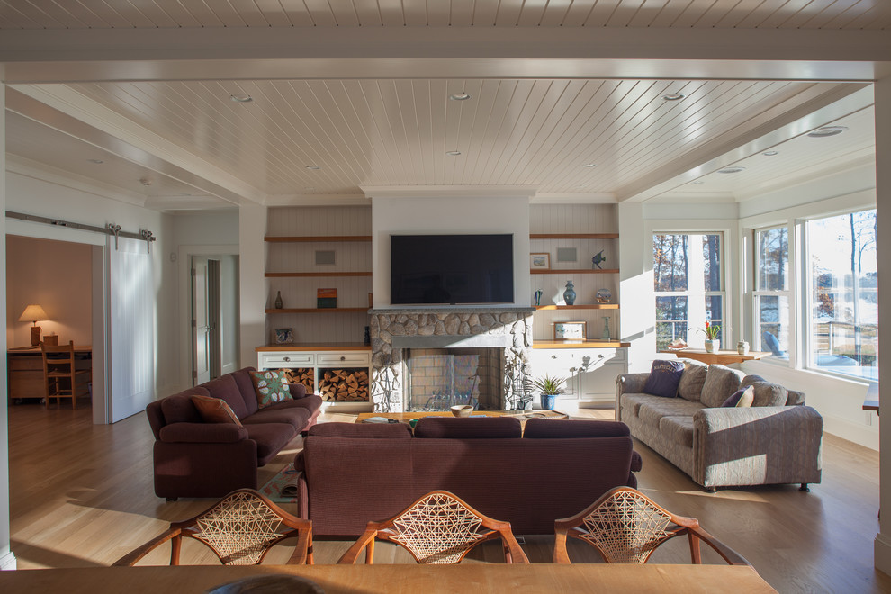 Inspiration for a medium sized beach style open plan living room in Boston with white walls, light hardwood flooring, a standard fireplace, a stone fireplace surround, a wall mounted tv and brown floors.