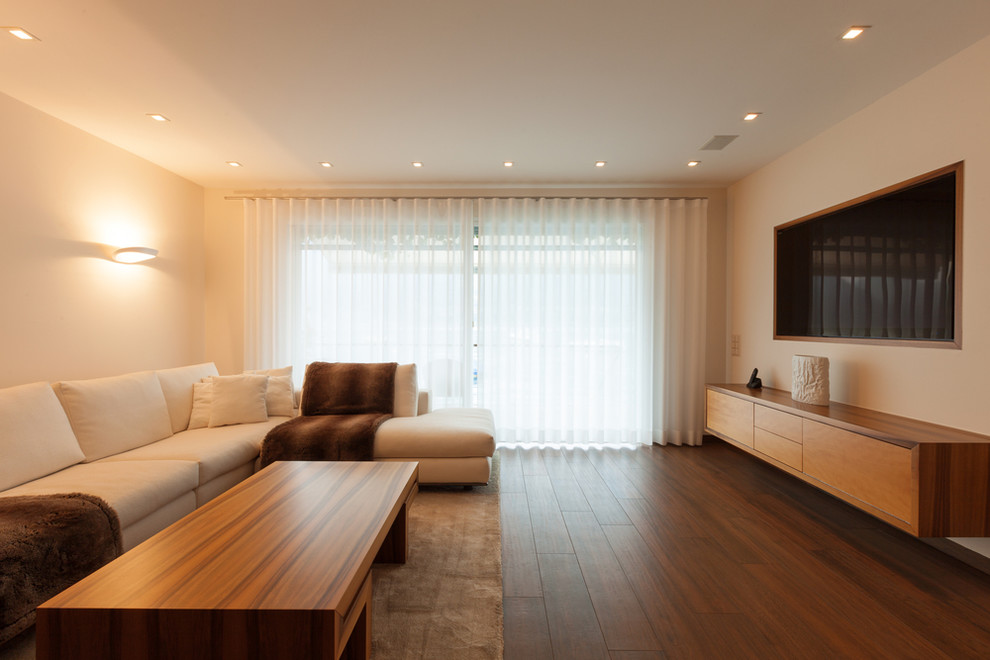 Foto de salón abierto actual de tamaño medio con paredes beige, suelo de madera oscura y pared multimedia