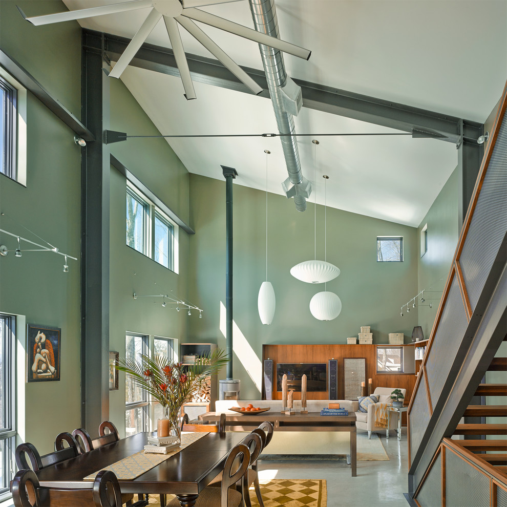 Modelo de salón abierto minimalista de tamaño medio con paredes verdes, suelo de cemento, estufa de leña y televisor colgado en la pared