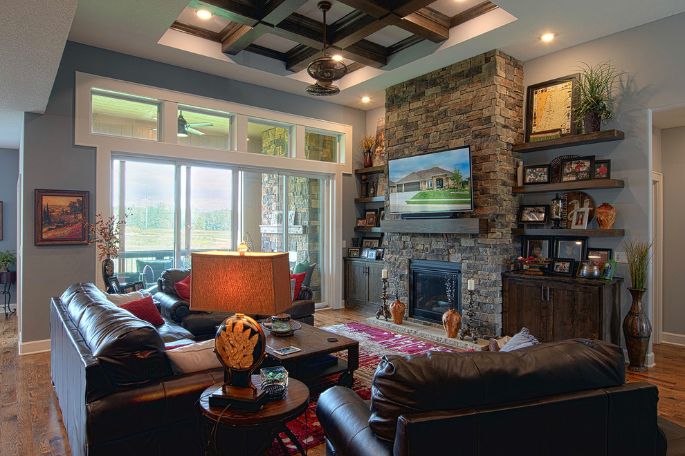 Aménagement d'un salon montagne ouvert avec un mur bleu, un sol en bois brun, une cheminée standard, un manteau de cheminée en pierre, un téléviseur fixé au mur et un sol marron.