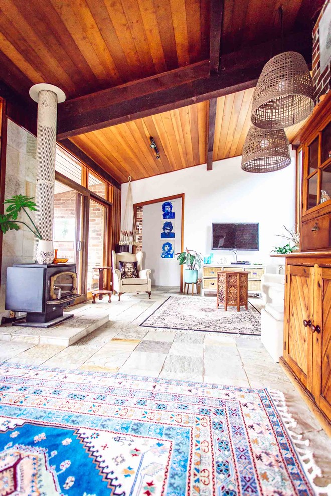 Immagine di un grande soggiorno tropicale chiuso con pareti bianche, pavimento in ardesia, stufa a legna, cornice del camino in pietra e TV a parete