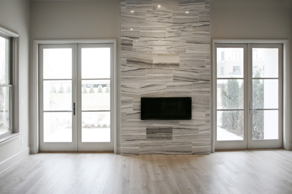 Пример оригинального дизайна: большая открытая гостиная комната в современном стиле с белыми стенами, светлым паркетным полом, горизонтальным камином и фасадом камина из камня без телевизора