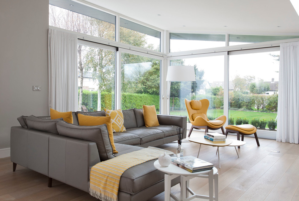 Large contemporary grey and yellow enclosed living room in Dublin with grey walls, light hardwood flooring, no fireplace and beige floors.