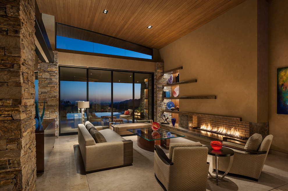 Expansive contemporary open plan living room in Phoenix with beige walls, medium hardwood flooring, a standard fireplace, a stone fireplace surround, a concealed tv and beige floors.