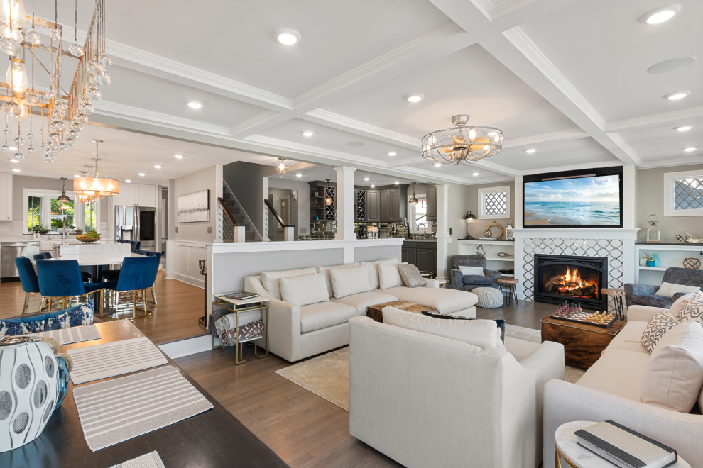 This is an example of a large traditional open plan living room in Milwaukee with a home bar, grey walls, light hardwood flooring, a standard fireplace, a tiled fireplace surround, a wall mounted tv, beige floors and a coffered ceiling.