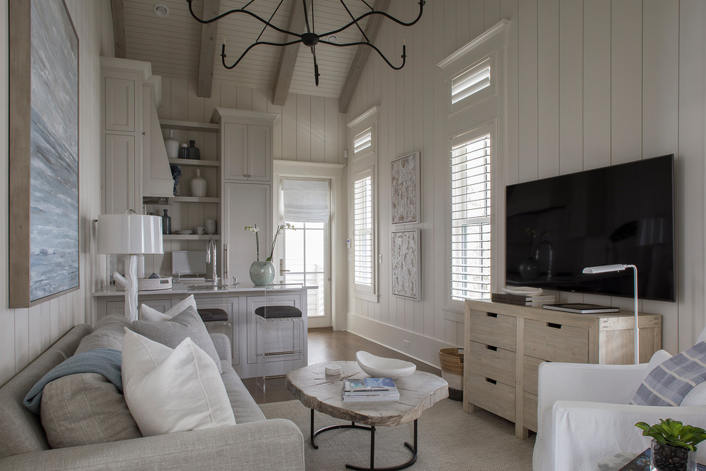 Diseño de salón abierto costero pequeño sin chimenea con paredes blancas, suelo de madera oscura, televisor colgado en la pared y suelo marrón