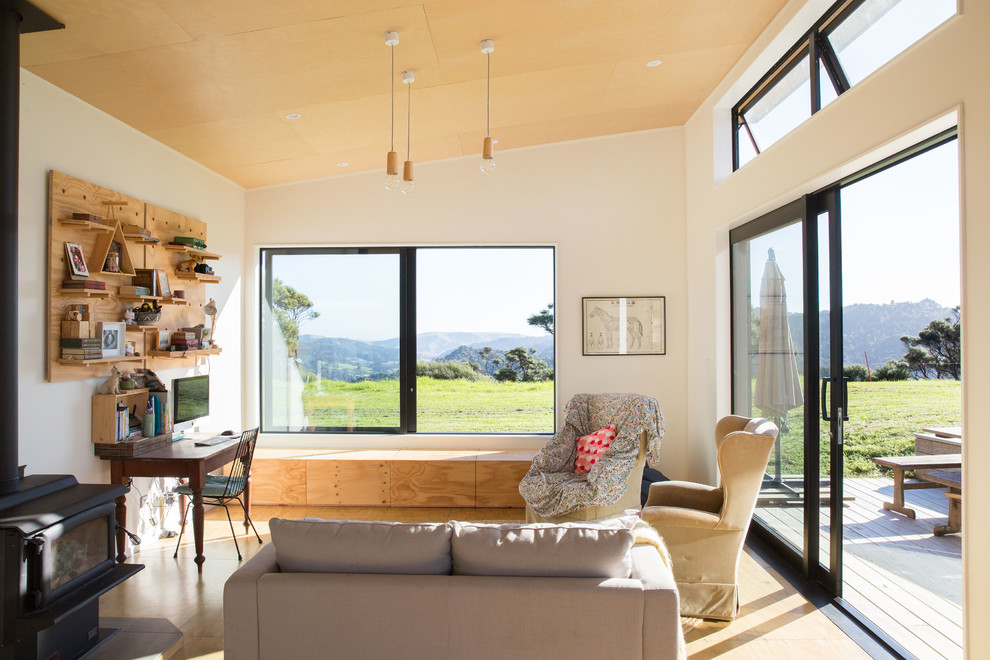 Offenes Skandinavisches Wohnzimmer mit weißer Wandfarbe, Sperrholzboden, Kaminofen und braunem Boden in Auckland