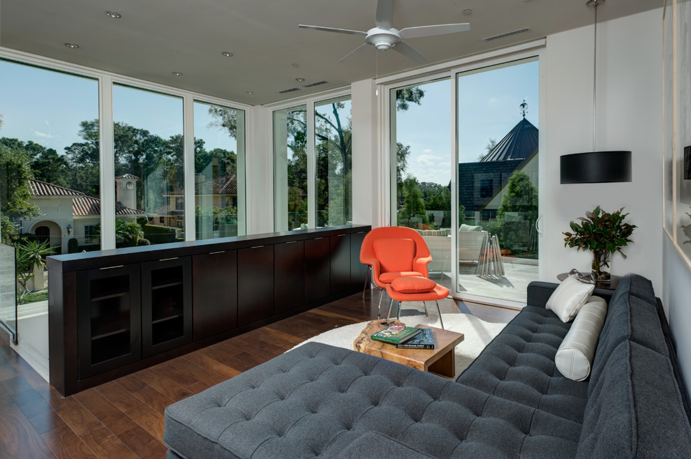 Modelo de salón tipo loft contemporáneo con paredes blancas, televisor retractable y suelo de madera en tonos medios