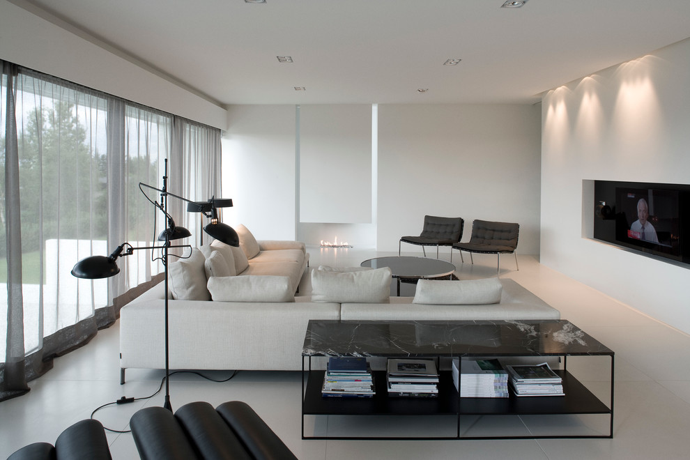 Свежая идея для дизайна: парадная, открытая гостиная комната в стиле модернизм с белыми стенами, стандартным камином, фасадом камина из штукатурки, телевизором на стене и серым полом - отличное фото интерьера