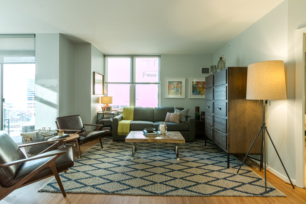 Cette image montre un grand salon minimaliste ouvert avec un mur gris, un sol en bois brun et un téléviseur dissimulé.