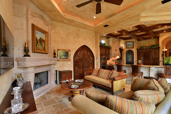 На фото: большая открытая гостиная комната в средиземноморском стиле с с книжными шкафами и полками, коричневыми стенами, полом из травертина, стандартным камином и фасадом камина из камня