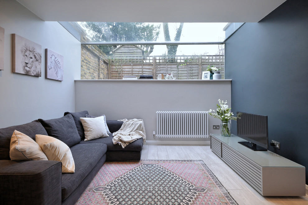 Diseño de salón contemporáneo con paredes grises, suelo de madera clara y televisor independiente