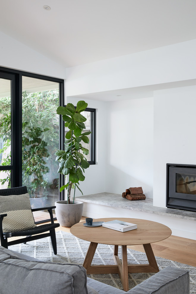 Diseño de salón abierto nórdico de tamaño medio con paredes blancas, suelo de madera clara, estufa de leña, marco de chimenea de yeso y suelo marrón