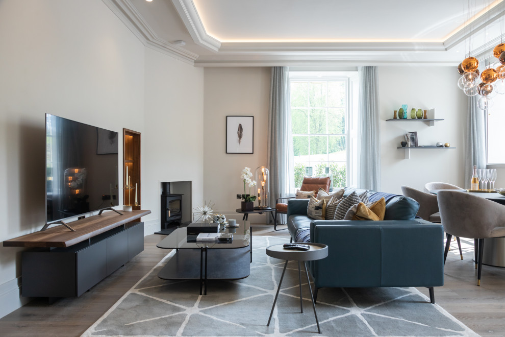 Идея дизайна: открытая гостиная комната в стиле неоклассика (современная классика) с белыми стенами, паркетным полом среднего тона, печью-буржуйкой, отдельно стоящим телевизором, коричневым полом и многоуровневым потолком