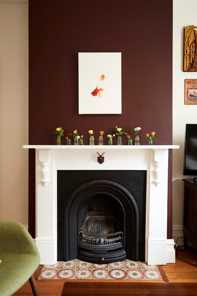 シドニーにあるお手頃価格のヴィクトリアン調のおしゃれな独立型リビング (紫の壁、磁器タイルの床、薪ストーブ、木材の暖炉まわり、赤い床) の写真