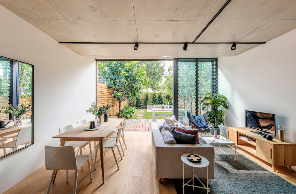 Offenes Modernes Wohnzimmer mit weißer Wandfarbe, braunem Holzboden, freistehendem TV und braunem Boden in Sydney