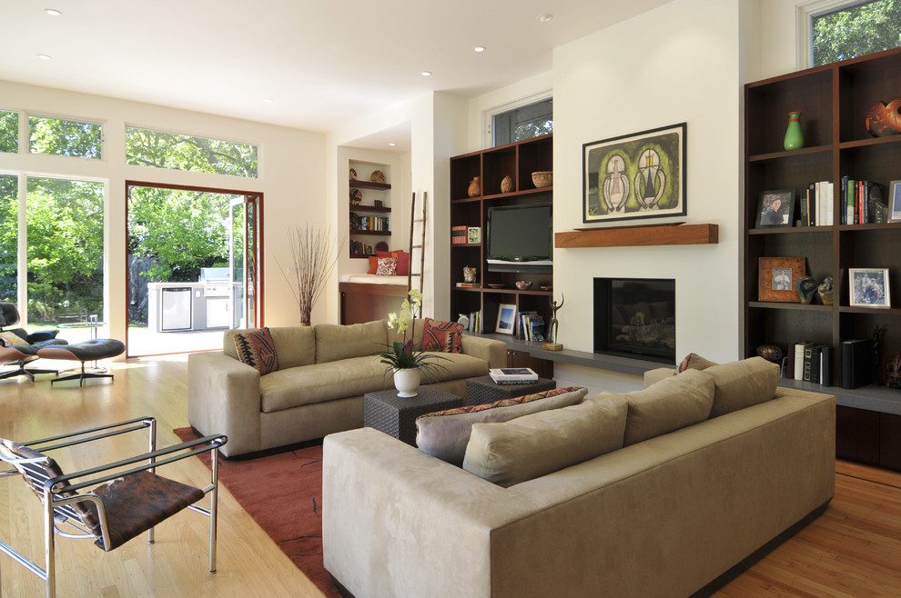 Contemporary open plan living room in San Francisco with a reading nook, a standard fireplace, white walls, medium hardwood flooring, a plastered fireplace surround and a built-in media unit.