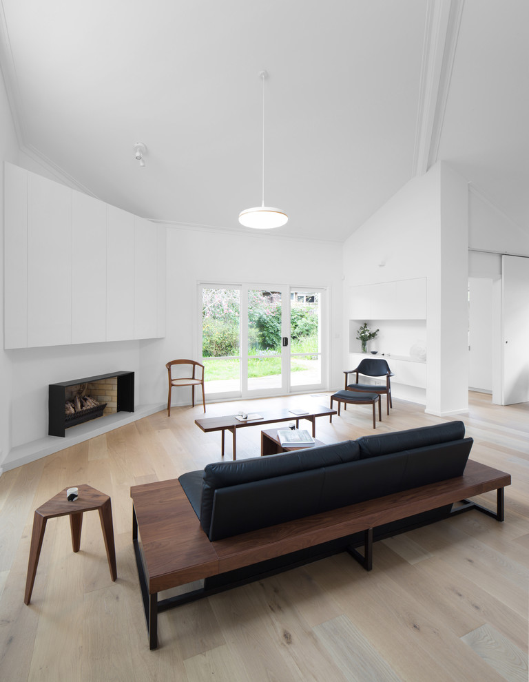 Inspiration pour un salon design avec un mur blanc, parquet clair, une cheminée standard, un sol beige et canapé noir.