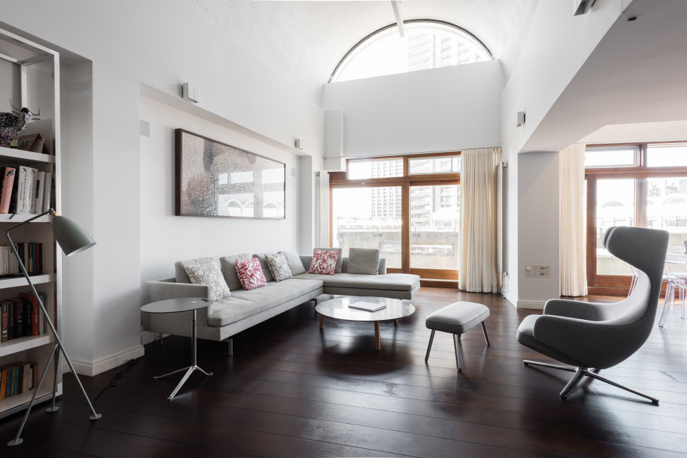 Modelo de salón abierto, abovedado y blanco actual grande sin chimenea y televisor con paredes blancas, suelo de madera oscura y suelo marrón