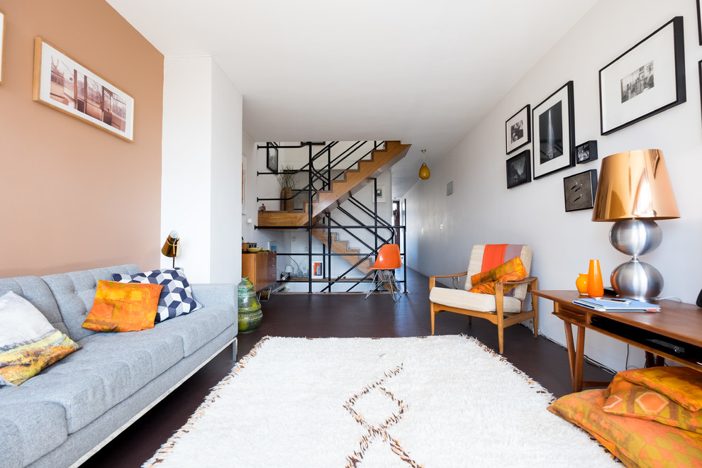 Offenes Modernes Wohnzimmer ohne Kamin mit oranger Wandfarbe und dunklem Holzboden in London