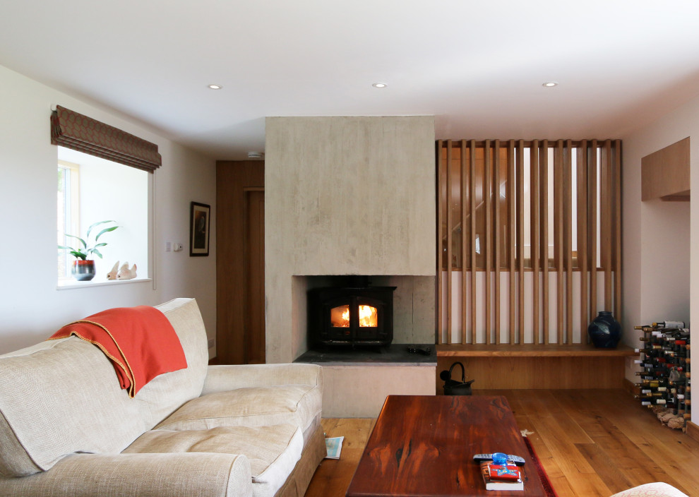 Mittelgroßes, Offenes Modernes Wohnzimmer mit weißer Wandfarbe, braunem Holzboden, Kaminofen, Kaminumrandung aus Beton und TV-Wand in Devon