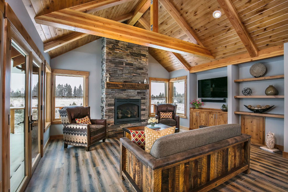 Mid-sized mountain style formal and open concept medium tone wood floor and brown floor living room photo in Other with gray walls, a standard fireplace, a stone fireplace and a wall-mounted tv