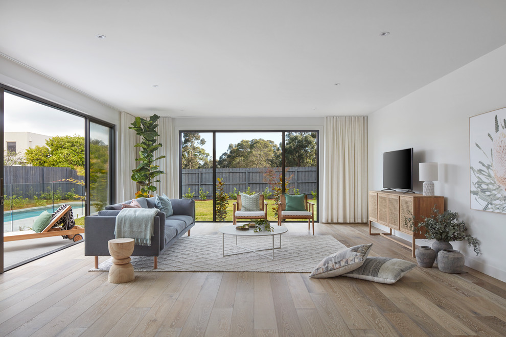 Cette image montre un salon design avec un mur blanc, parquet clair, un téléviseur indépendant et un sol marron.