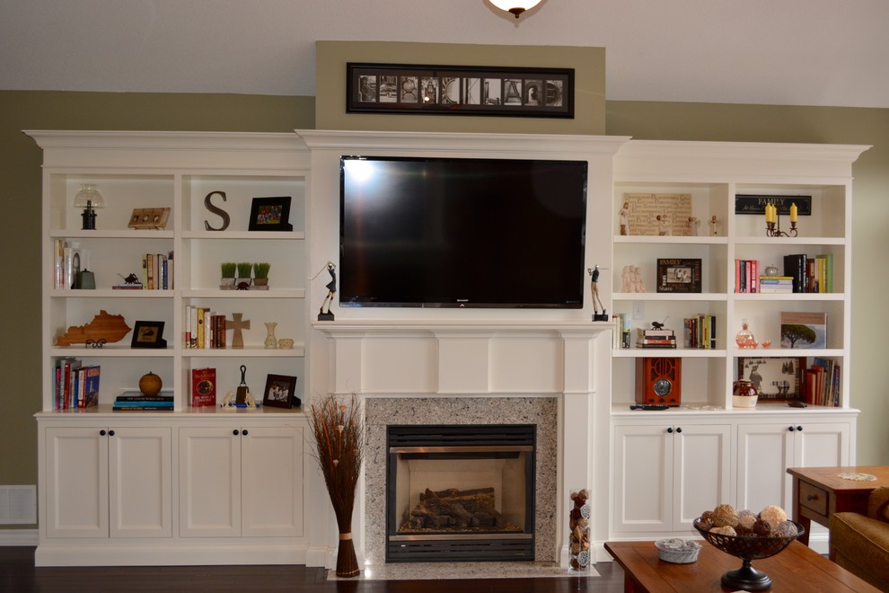 На фото: открытая гостиная комната среднего размера в стиле неоклассика (современная классика) с с книжными шкафами и полками, бежевыми стенами, темным паркетным полом, стандартным камином, фасадом камина из дерева и телевизором на стене с