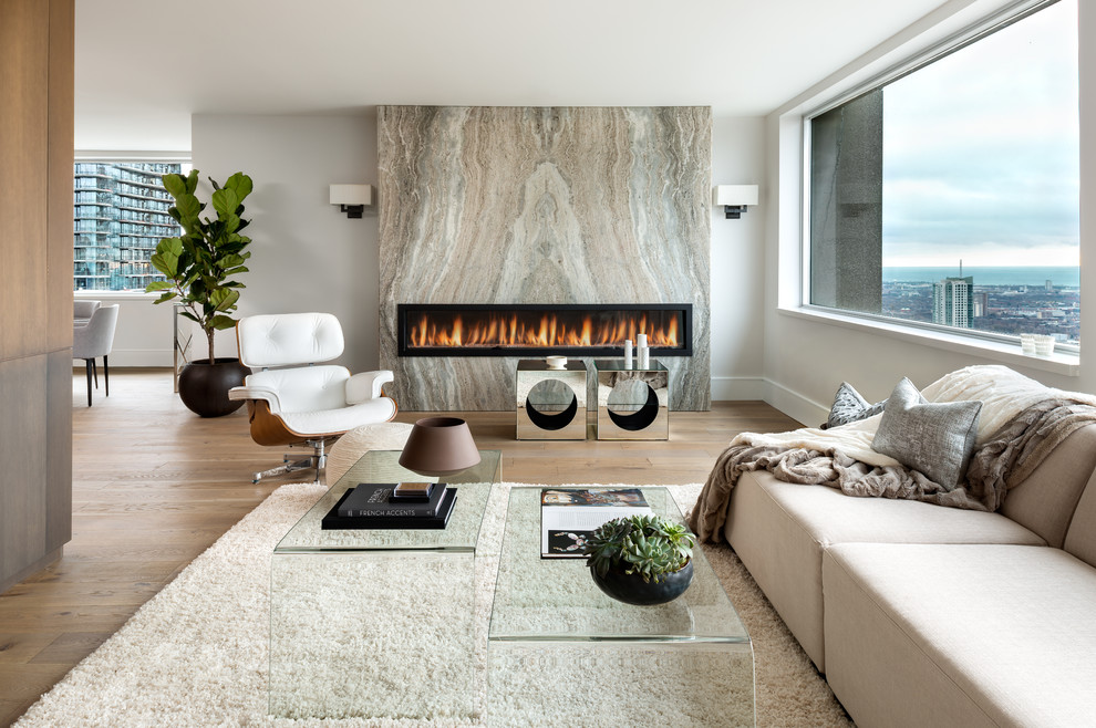 Diseño de salón abierto contemporáneo sin televisor con paredes blancas, marco de chimenea de piedra, suelo de madera clara y chimenea lineal