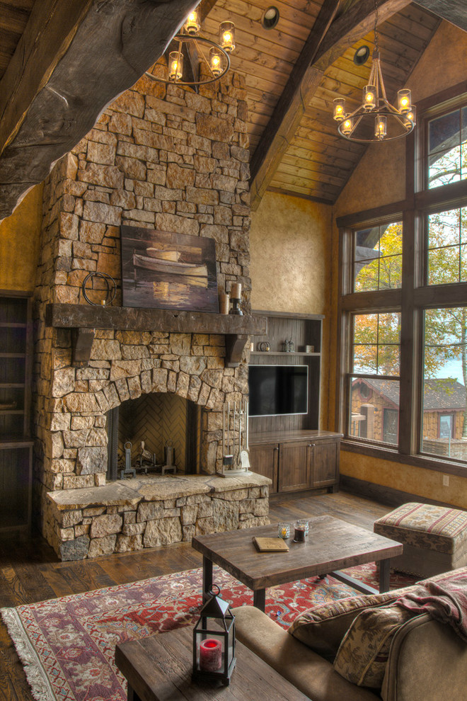 Aménagement d'un salon montagne de taille moyenne et ouvert avec un sol en bois brun, une cheminée standard, un manteau de cheminée en pierre et un téléviseur fixé au mur.