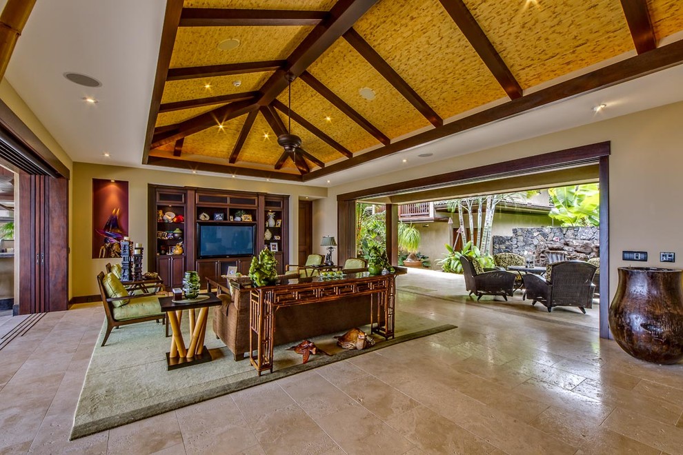Immagine di un ampio soggiorno tropicale aperto con pareti beige, pavimento in travertino, nessun camino e parete attrezzata
