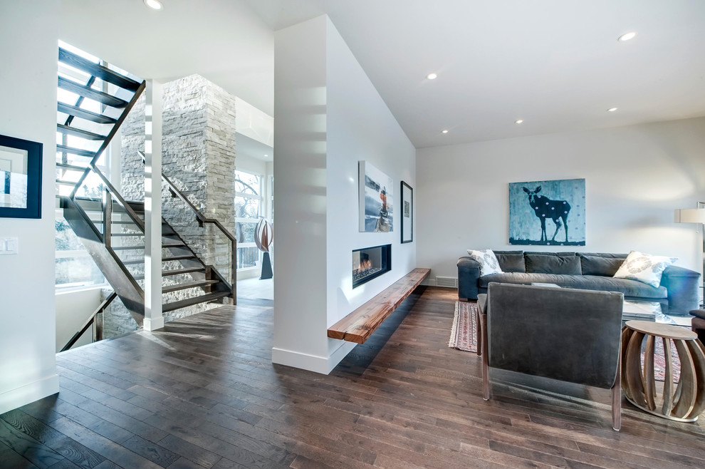 Example of a large minimalist formal and open concept medium tone wood floor living room design in Calgary with white walls, a ribbon fireplace, a plaster fireplace and no tv