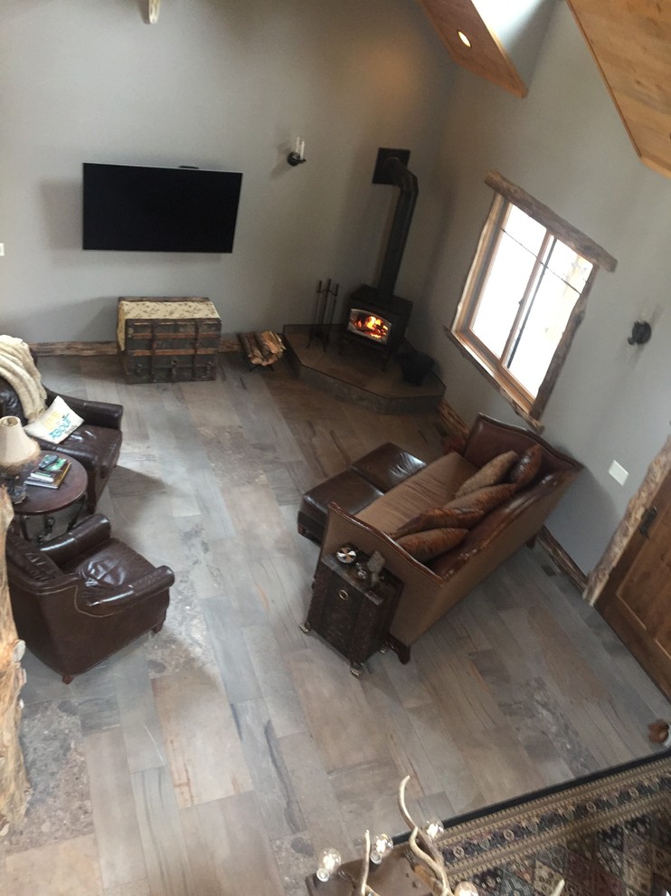 Rustikales Wohnzimmer mit grauer Wandfarbe, Porzellan-Bodenfliesen, Kaminofen, TV-Wand und grauem Boden in Sonstige