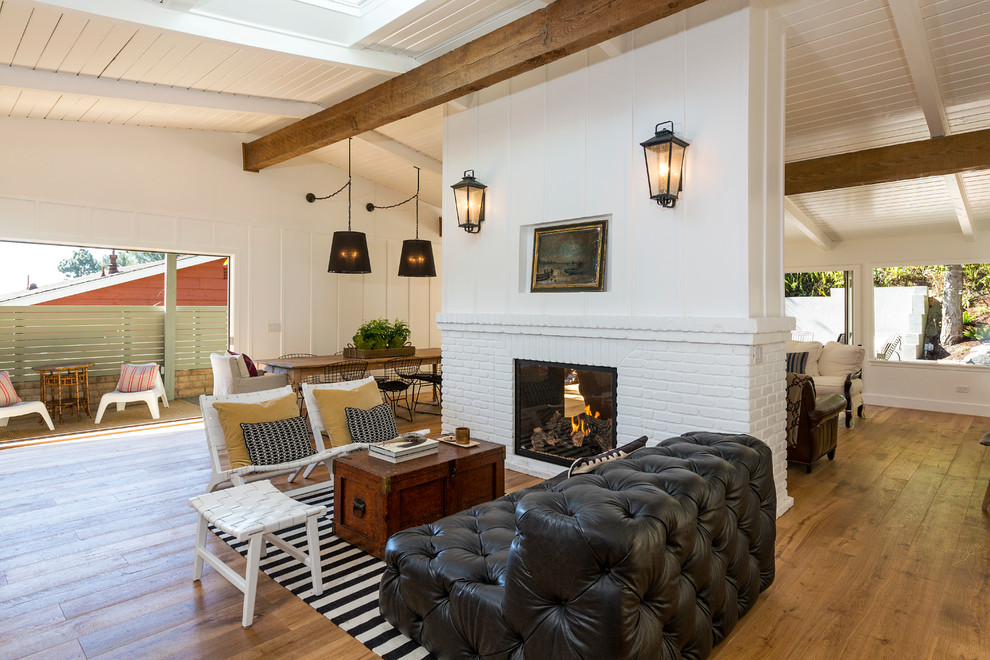Diseño de salón para visitas abierto costero con paredes blancas, suelo de madera en tonos medios y chimenea de doble cara