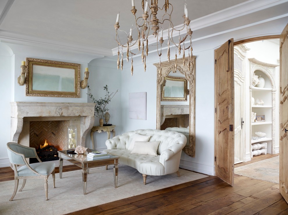Aménagement d'un salon avec un mur blanc, un sol en bois brun, une cheminée standard et un manteau de cheminée en pierre.