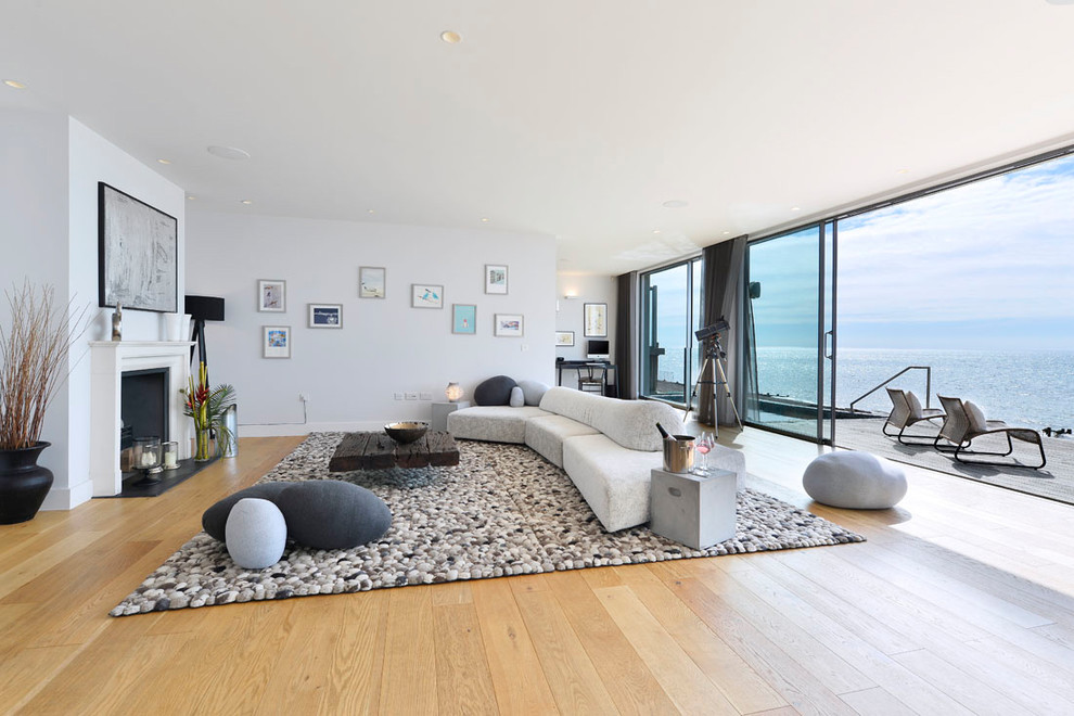 Mittelgroßes, Offenes Maritimes Wohnzimmer mit weißer Wandfarbe, hellem Holzboden, Kamin, Kaminumrandung aus Stein und beigem Boden in London