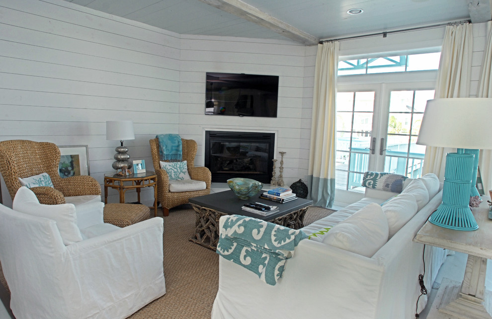 Imagen de salón abierto costero con paredes blancas, marco de chimenea de madera y televisor colgado en la pared