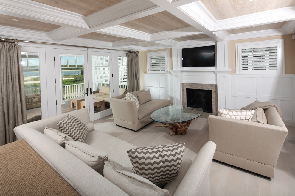 Ejemplo de salón abierto costero con paredes beige, suelo de madera clara, todas las chimeneas, marco de chimenea de piedra y televisor colgado en la pared