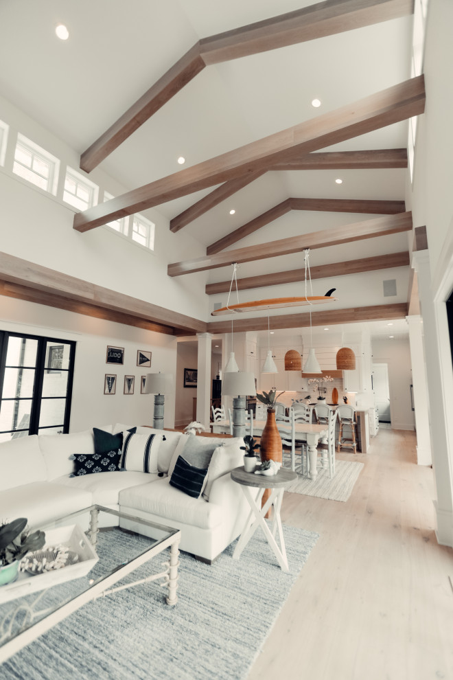 Пример оригинального дизайна: огромная открытая гостиная комната в морском стиле с белыми стенами, светлым паркетным полом, стандартным камином, фасадом камина из плитки, телевизором на стене, бежевым полом и балками на потолке