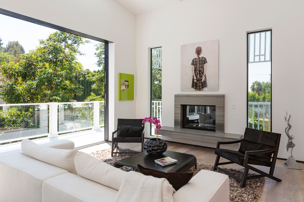 Modernes Wohnzimmer mit weißer Wandfarbe, Kamin, Kaminumrandung aus Stein und hellem Holzboden in Los Angeles