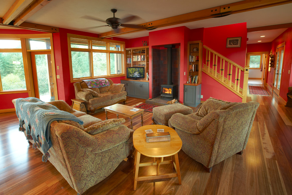 Пример оригинального дизайна: открытая гостиная комната среднего размера в стиле кантри с красными стенами, паркетным полом среднего тона, печью-буржуйкой, фасадом камина из плитки и отдельно стоящим телевизором