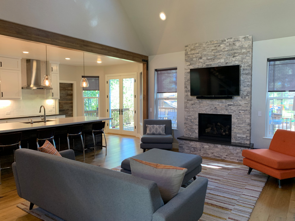 Example of a farmhouse open concept light wood floor living room design in Phoenix with white walls, a standard fireplace, a stone fireplace and a wall-mounted tv