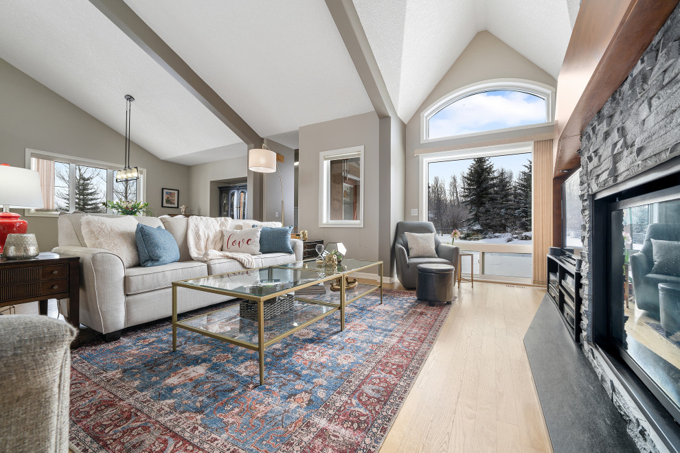 Large traditional open plan living room in Calgary with grey walls, medium hardwood flooring, a standard fireplace, a stone fireplace surround and a freestanding tv.