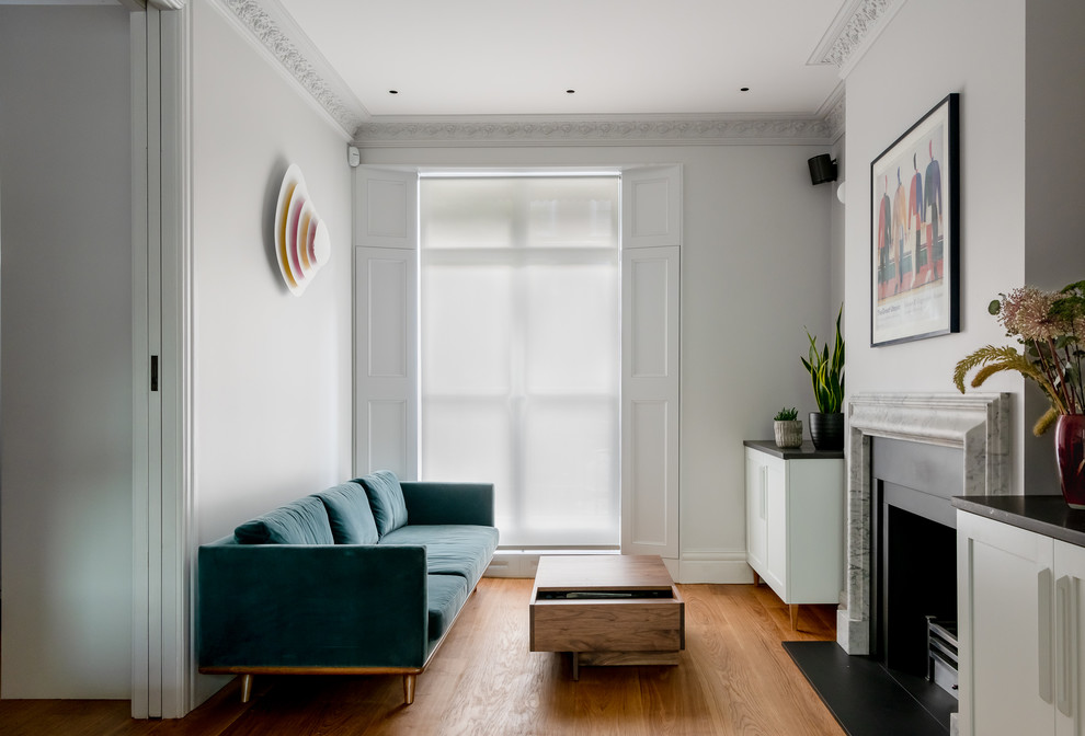 This is an example of a contemporary formal enclosed living room in London with white walls, medium hardwood flooring, a standard fireplace and no tv.