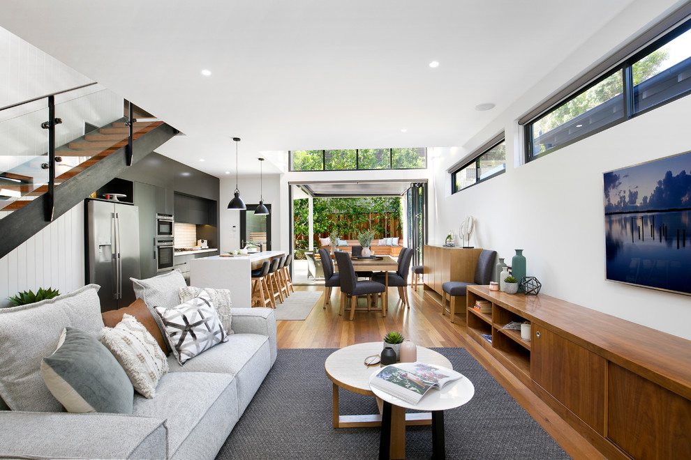 Design ideas for a contemporary open plan living room in Sydney with white walls, medium hardwood flooring, no fireplace, a wall mounted tv and brown floors.