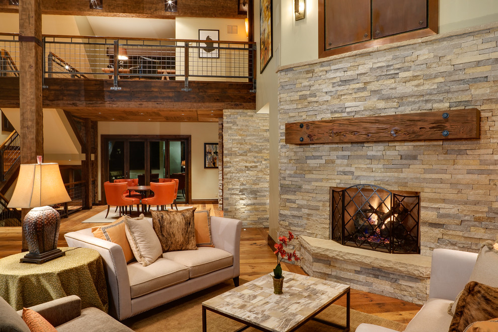 Offenes Rustikales Wohnzimmer mit beiger Wandfarbe, braunem Holzboden, Kamin und Kaminumrandung aus Stein in Denver