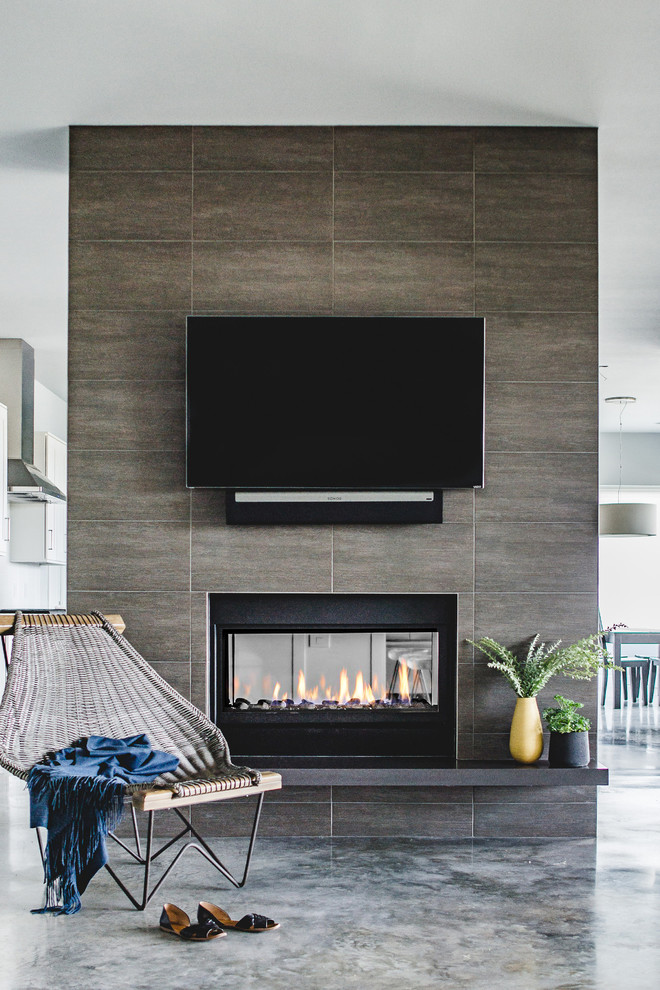オースティンにあるお手頃価格の中くらいなコンテンポラリースタイルのおしゃれなLDK (グレーの壁、コンクリートの床、両方向型暖炉、壁掛け型テレビ、タイルの暖炉まわり) の写真