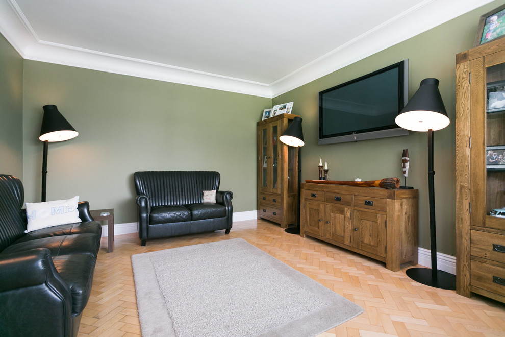 Cette image montre un salon traditionnel de taille moyenne et fermé avec un mur vert, parquet clair et un téléviseur fixé au mur.